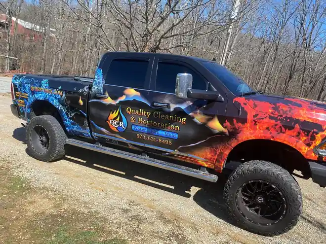 The flame and water wrapped QCR truck on a wooded gravel drive