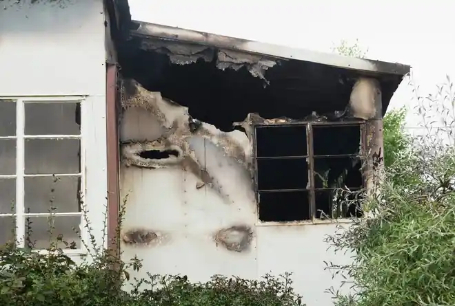 White house with a burned-out window and scorched eaves after a fire