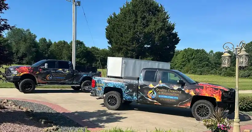 Two flame and water wrapped QCR trucks on a driveway under a blue sky