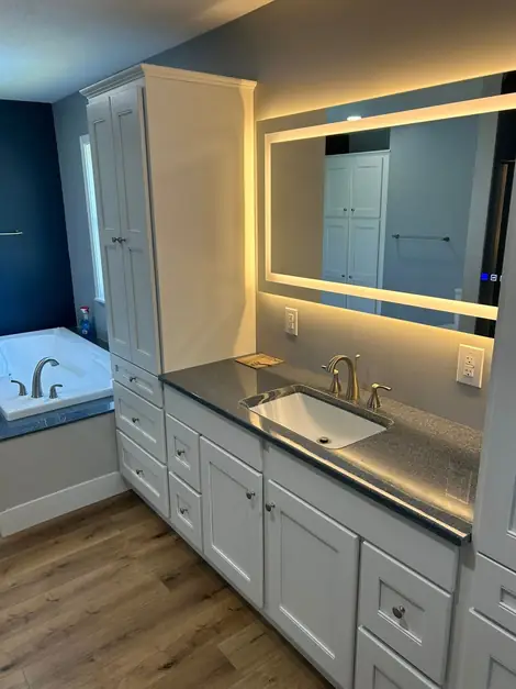 Vanity and tall cabinet under a backlit mirror