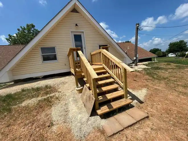 Yellow-sided A-frame house with new timber steps under a blue sky