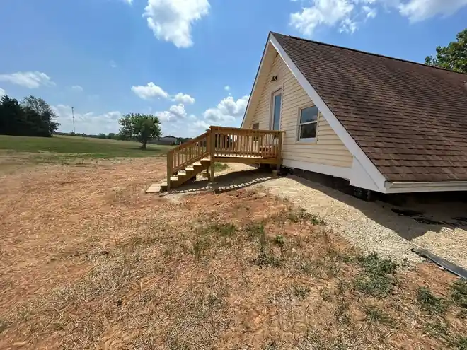 Side of the A-frame house with its new deck in an open field