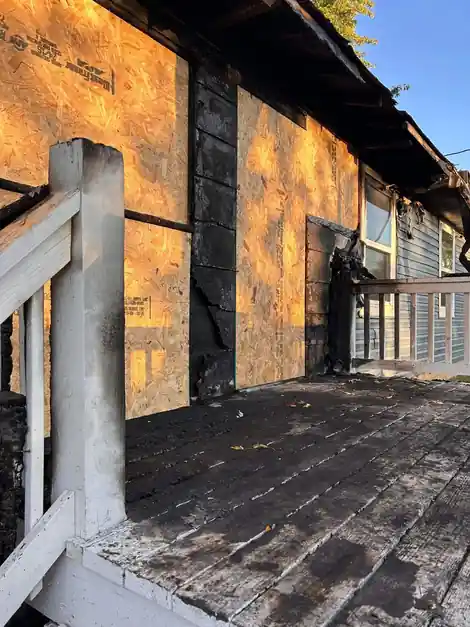 Fire-damaged porch wall boarded up with OSB