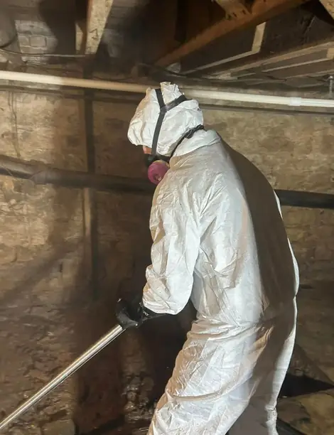 Technician in a full white suit and respirator working in a stone-walled crawlspace